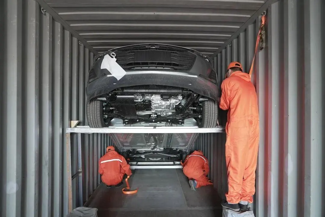 Workers securing a vehicle on a loading rack inside a shipping container